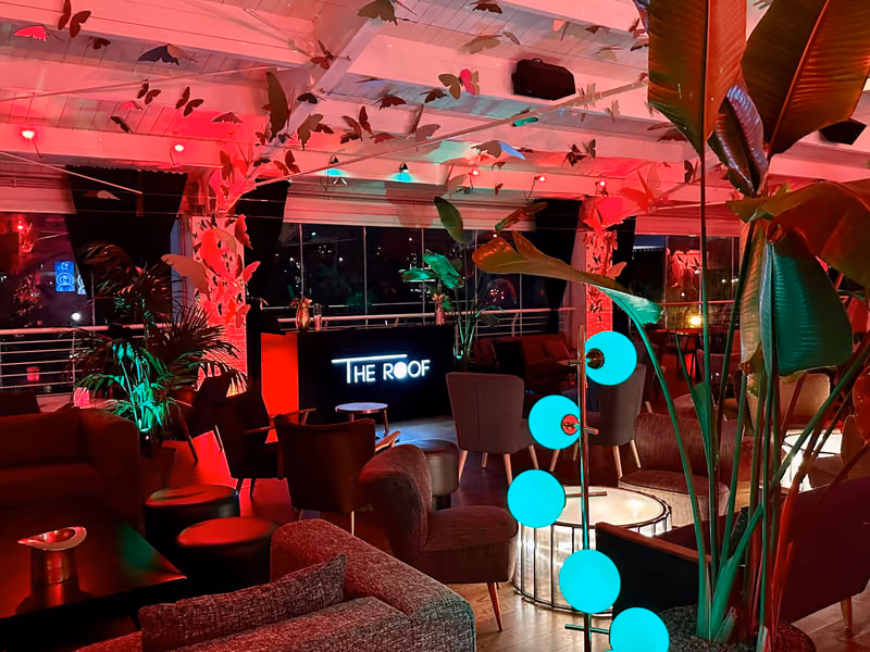 Il salotto di The Roof con luci rosse, piante tropicali e l'insegna luminosa