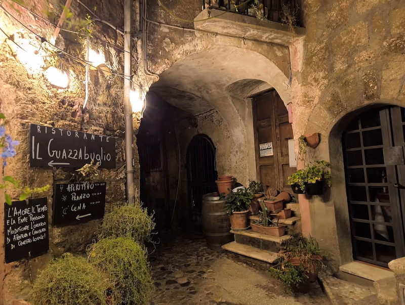 L'ingresso nel vicolo con l'insegna e la lavagna, di sera